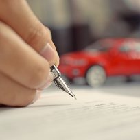 Man signing car insurance document. Writing signature on contract or agreement. Buying or selling new or used vehicle.