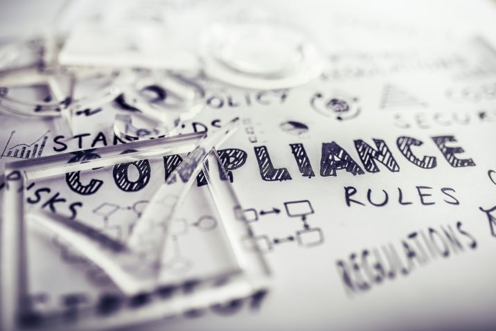 Transparent check mark over compliance related icons and words handwritten on white papers