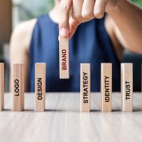 Businesswoman hand placing or pulling wooden Dominoes with BRAND text. and Marketing, Advertising, Logo, Design, Strategy, Identity, Trust and Values. Product development concept