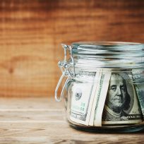 Dollar bills in glass jar on rustic table. Saving money concept.