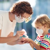 Family with kids in face mask in shopping mall or airport. Mother and child wear facemask during coronavirus and flu outbreak. Virus and illness protection, hand sanitizer in public crowded place.