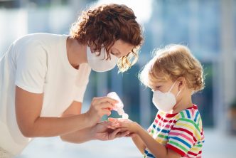 Family with kids in face mask in shopping mall or airport. Mother and child wear facemask during coronavirus and flu outbreak. Virus and illness protection, hand sanitizer in public crowded place.