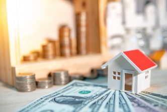 Property or real estate investment concept. Home mortgage loan rate. Saving money for future retirement. Miniature house model with stacked coins and dollar currency banknotes on wooden table.