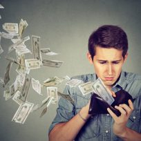 Man looking at wallet with money dollars flying away