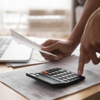 African woman holding paper bills using calculator, close up view