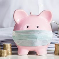 Businessman Calculating Invoice With Piggybank And Coins At Desk