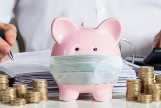 Businessman Calculating Invoice With Piggybank And Coins At Desk